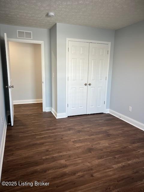 unfurnished bedroom featuring a textured ceiling, a closet, and dark hardwood / wood-style flooring