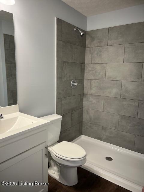 bathroom featuring toilet, vanity, wood-type flooring, and tiled shower