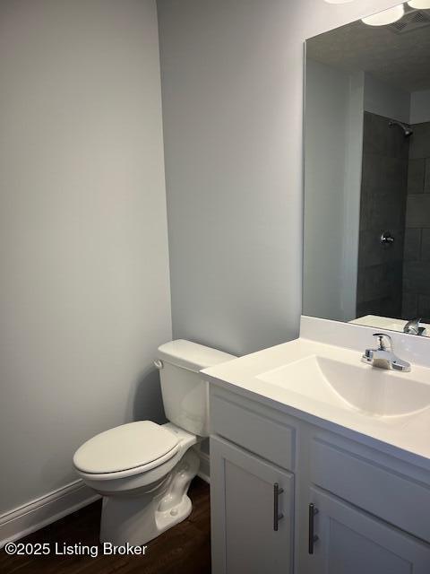 bathroom with toilet, a tile shower, hardwood / wood-style flooring, and vanity