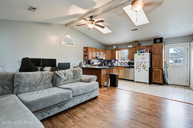 living room with a textured ceiling, ceiling fan, vaulted ceiling with skylight, and light hardwood / wood-style flooring