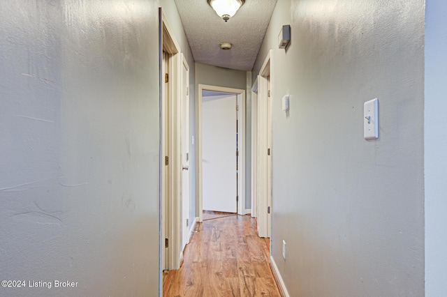 hall with a textured ceiling and light wood-type flooring