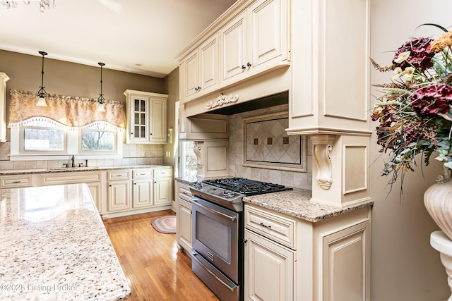 kitchen with sink, light stone counters, stainless steel gas range, backsplash, and hanging light fixtures