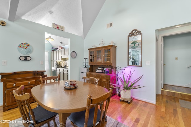 dining area with high vaulted ceiling and light wood-type flooring