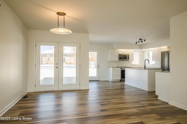 interior space featuring stainless steel appliances, dark wood-type flooring, french doors, white cabinetry, and decorative light fixtures