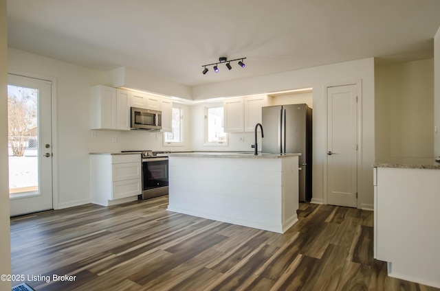 kitchen featuring appliances with stainless steel finishes, a center island, light stone countertops, dark wood-type flooring, and white cabinetry