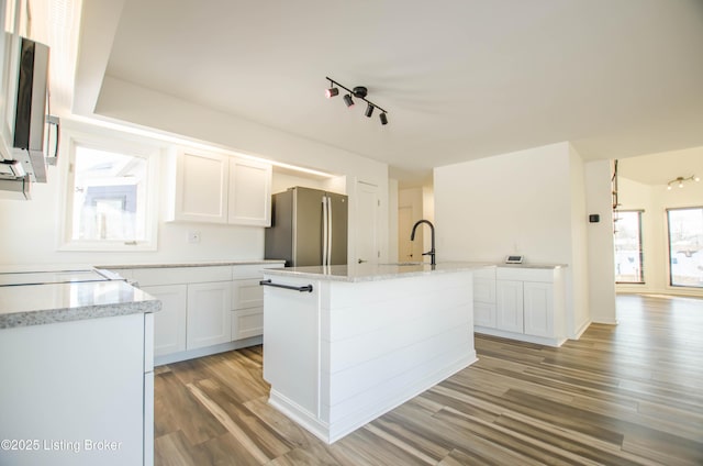 kitchen with white cabinetry, stainless steel appliances, an island with sink, light stone counters, and light hardwood / wood-style flooring