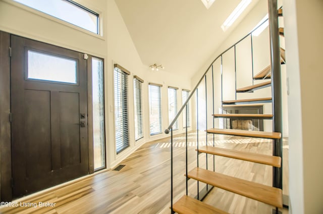 foyer featuring high vaulted ceiling, a skylight, plenty of natural light, and light hardwood / wood-style flooring