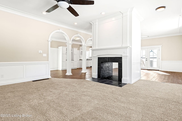 unfurnished living room with dark colored carpet, crown molding, a multi sided fireplace, and ceiling fan