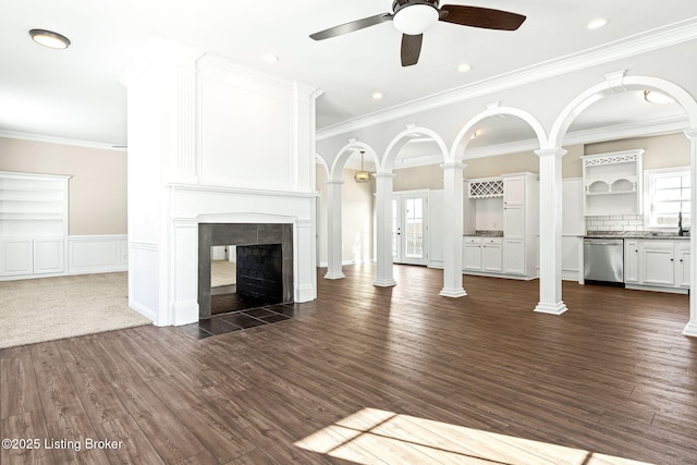 unfurnished living room featuring dark wood-type flooring, ornate columns, ornamental molding, ceiling fan, and a tiled fireplace