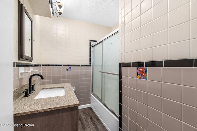 bathroom with wood-type flooring, shower / bath combination with glass door, a textured ceiling, tile walls, and vanity