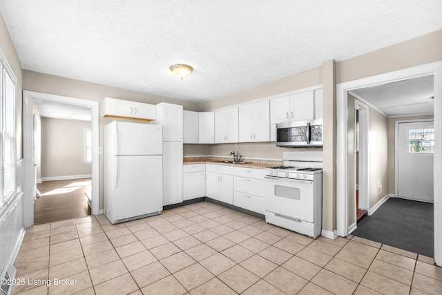 kitchen featuring sink, a textured ceiling, light tile patterned floors, white appliances, and white cabinets