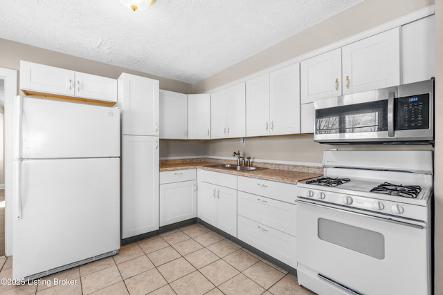 kitchen featuring white cabinetry, sink, light tile patterned floors, white appliances, and a textured ceiling