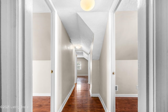 corridor featuring lofted ceiling, a textured ceiling, and dark hardwood / wood-style flooring