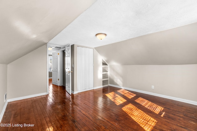 bonus room with vaulted ceiling, dark wood-type flooring, a textured ceiling, and built in shelves