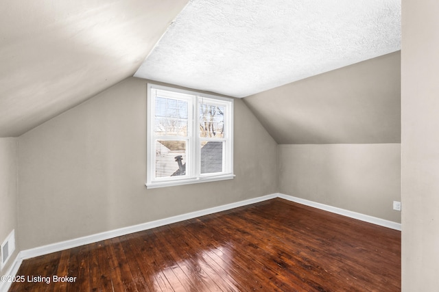 additional living space featuring hardwood / wood-style flooring, vaulted ceiling, and a textured ceiling