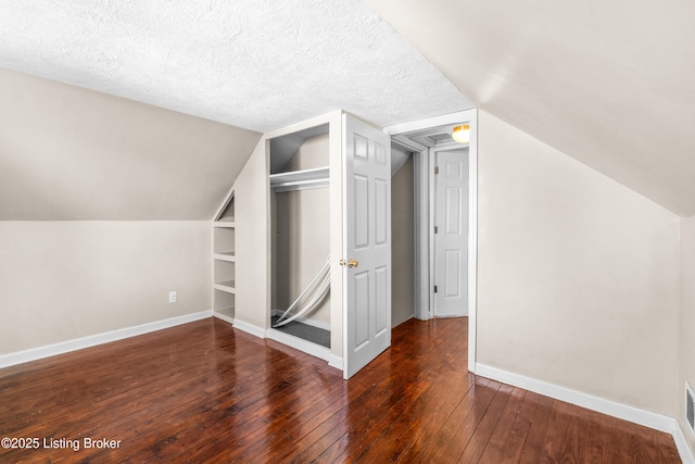 bonus room featuring dark wood-type flooring, built in features, a textured ceiling, and vaulted ceiling