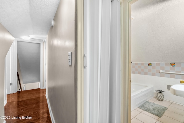 bathroom with tile patterned flooring, tile walls, a tub, and a textured ceiling