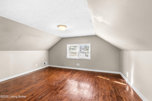 additional living space with dark hardwood / wood-style flooring, vaulted ceiling, and a textured ceiling