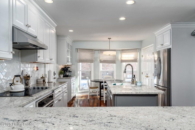 kitchen with a center island with sink, stainless steel refrigerator with ice dispenser, black electric stovetop, wall oven, and decorative backsplash