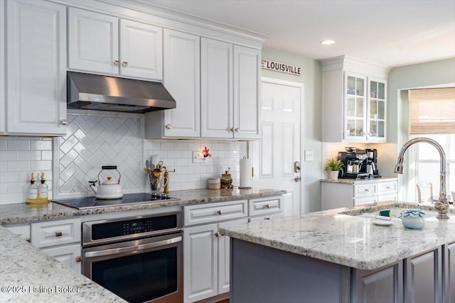 kitchen with black electric stovetop, decorative backsplash, sink, stainless steel oven, and white cabinets