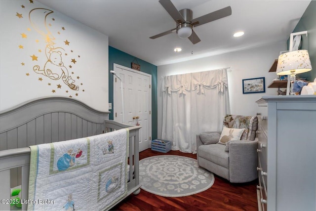 bedroom featuring ceiling fan, dark hardwood / wood-style flooring, and a nursery area