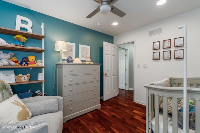 bedroom with ceiling fan, a nursery area, and dark hardwood / wood-style flooring