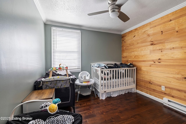 bedroom with ceiling fan, a nursery area, wooden walls, a textured ceiling, and a baseboard radiator