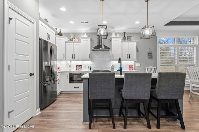 kitchen featuring a kitchen island with sink, ornamental molding, black fridge, white cabinetry, and decorative light fixtures