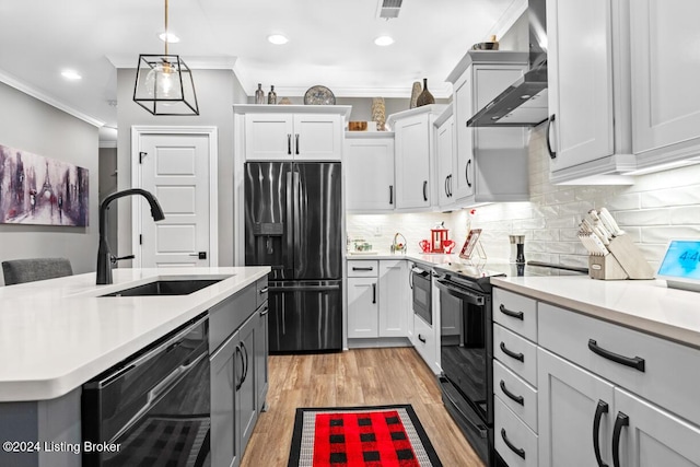 kitchen featuring black appliances, light wood-type flooring, pendant lighting, sink, and wall chimney range hood