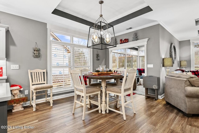 dining area featuring an inviting chandelier, a raised ceiling, ornamental molding, and wood-type flooring