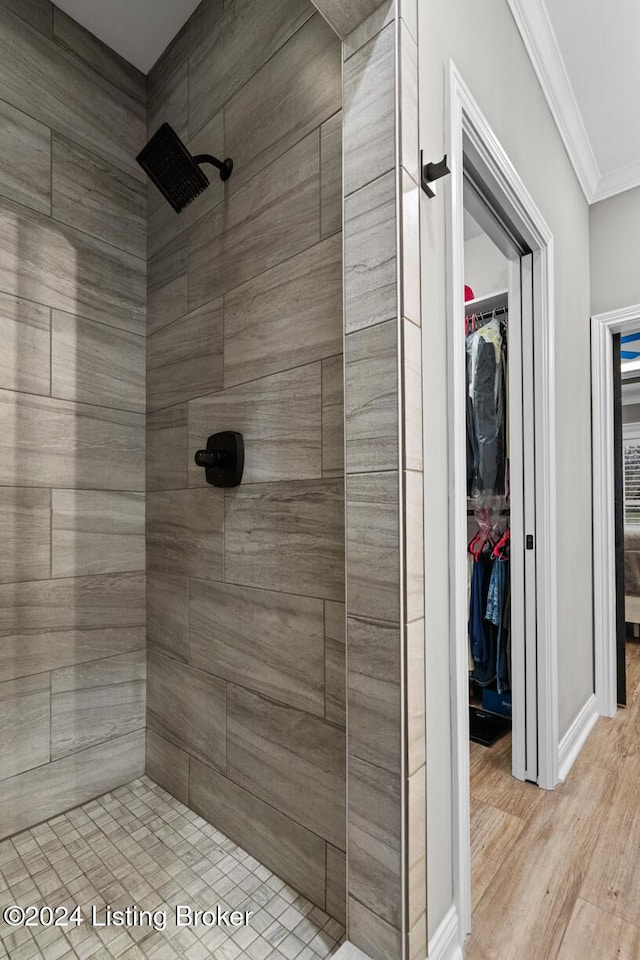 bathroom with a tile shower, wood-type flooring, and ornamental molding