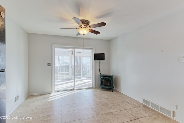 unfurnished room featuring ceiling fan, a wood stove, and light tile patterned floors