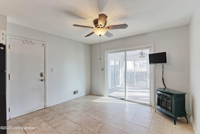 unfurnished living room featuring ceiling fan, light tile patterned flooring, and a wood stove