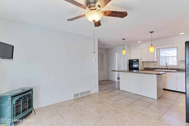 kitchen with white cabinets, sink, hanging light fixtures, a wood stove, and oven