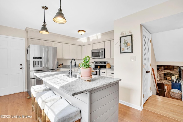 kitchen featuring a kitchen island with sink, stainless steel appliances, white cabinets, decorative light fixtures, and sink