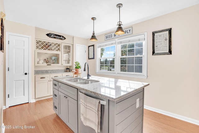 kitchen featuring sink, decorative light fixtures, dishwasher, light hardwood / wood-style flooring, and a kitchen island with sink