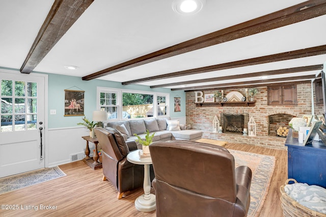 living room with a brick fireplace, light wood-type flooring, and beamed ceiling