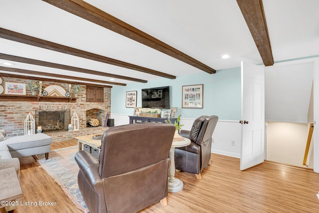 living room featuring a brick fireplace, light wood-type flooring, and beamed ceiling