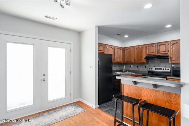 kitchen featuring a breakfast bar area, backsplash, electric range, black fridge, and french doors