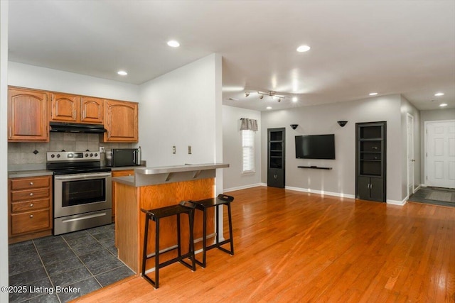 kitchen featuring stainless steel electric stove, dark hardwood / wood-style floors, tasteful backsplash, a kitchen bar, and a center island