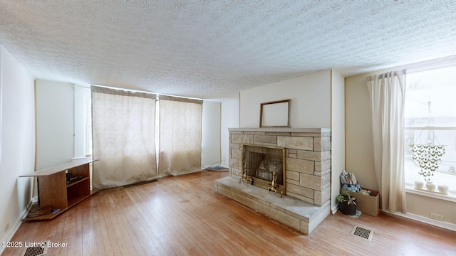 unfurnished living room featuring light hardwood / wood-style floors, a textured ceiling, and a stone fireplace