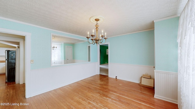 unfurnished room featuring a textured ceiling, ornamental molding, a chandelier, and light wood-type flooring