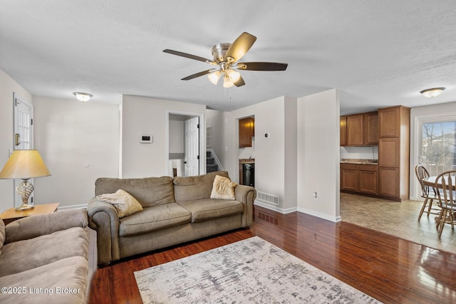 living room with ceiling fan, dark wood-type flooring, and a textured ceiling