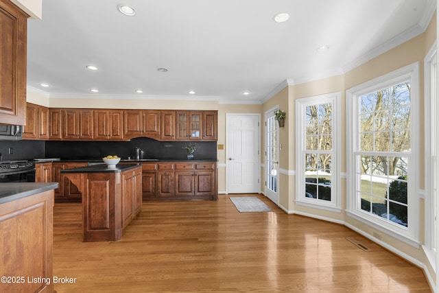 kitchen with a center island, backsplash, black range, light wood-type flooring, and crown molding