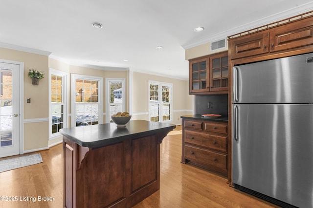 kitchen with stainless steel fridge, a kitchen breakfast bar, ornamental molding, light hardwood / wood-style flooring, and a center island