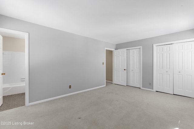 unfurnished bedroom featuring ensuite bathroom, light colored carpet, and multiple closets