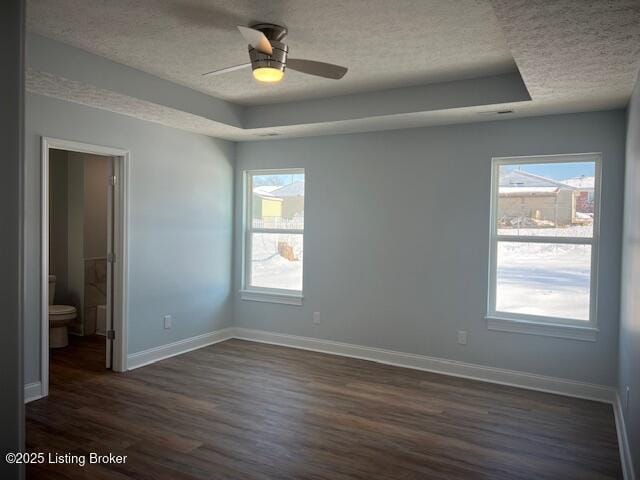 empty room with a textured ceiling, dark wood-type flooring, a tray ceiling, and ceiling fan