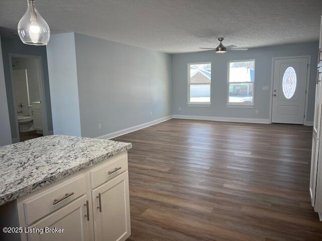 interior space featuring decorative light fixtures, ceiling fan, dark hardwood / wood-style floors, light stone countertops, and white cabinets