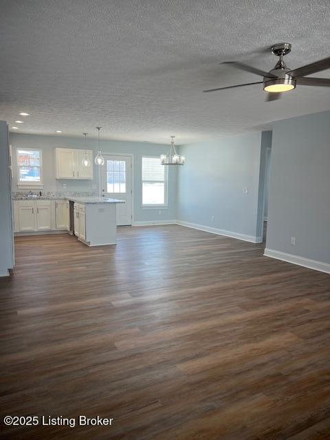 unfurnished living room with dark wood-type flooring, ceiling fan with notable chandelier, and a textured ceiling