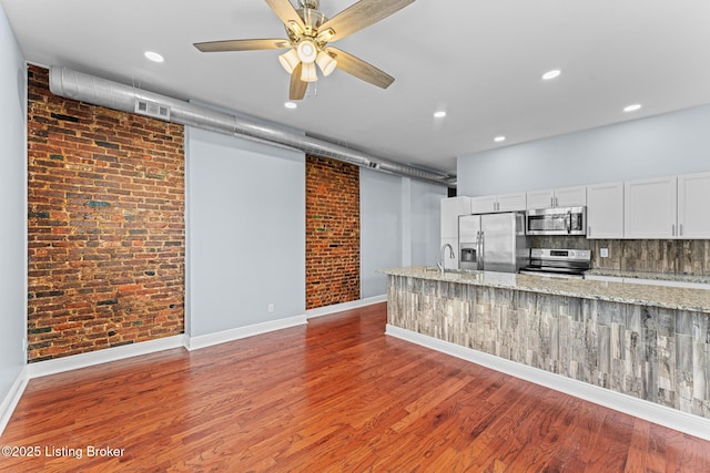 kitchen featuring white cabinets, hardwood / wood-style flooring, light stone countertops, brick wall, and appliances with stainless steel finishes